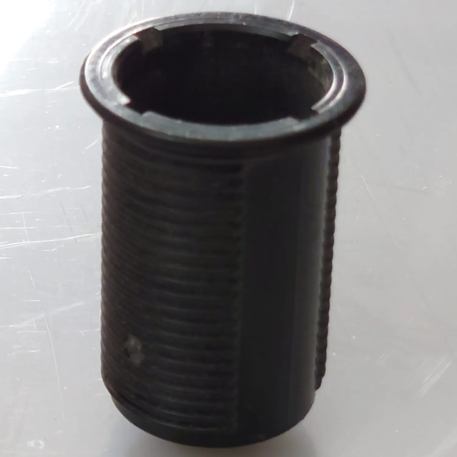 Pneumatisk knapp sedd rakt uppifrån, cylindrisk hylsa i metall med rund tryckknapp centrerad i mitten.